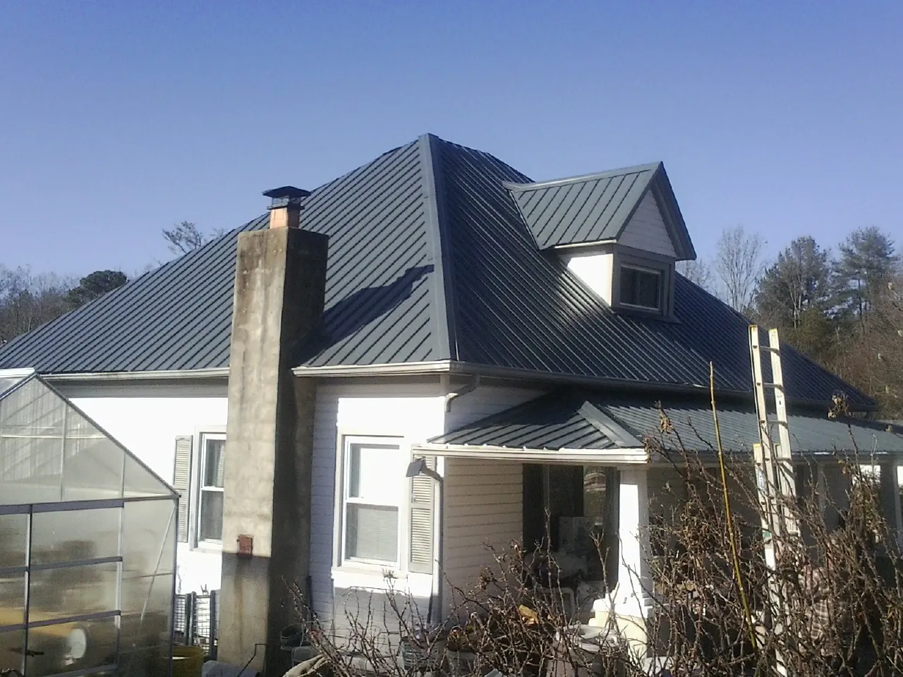 Dark blue standing seam metal roof on a white farmhouse with dormer — Slate & Tile Roof Repair by Roofing Brothers in Stevens