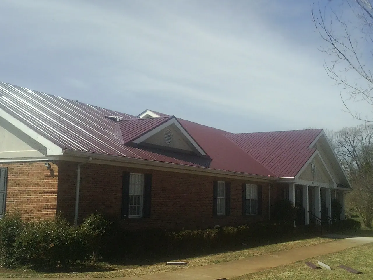 Red metal roof with gabled entries on a long brick building, from a Hail Damage Roof Repair job in Stevens