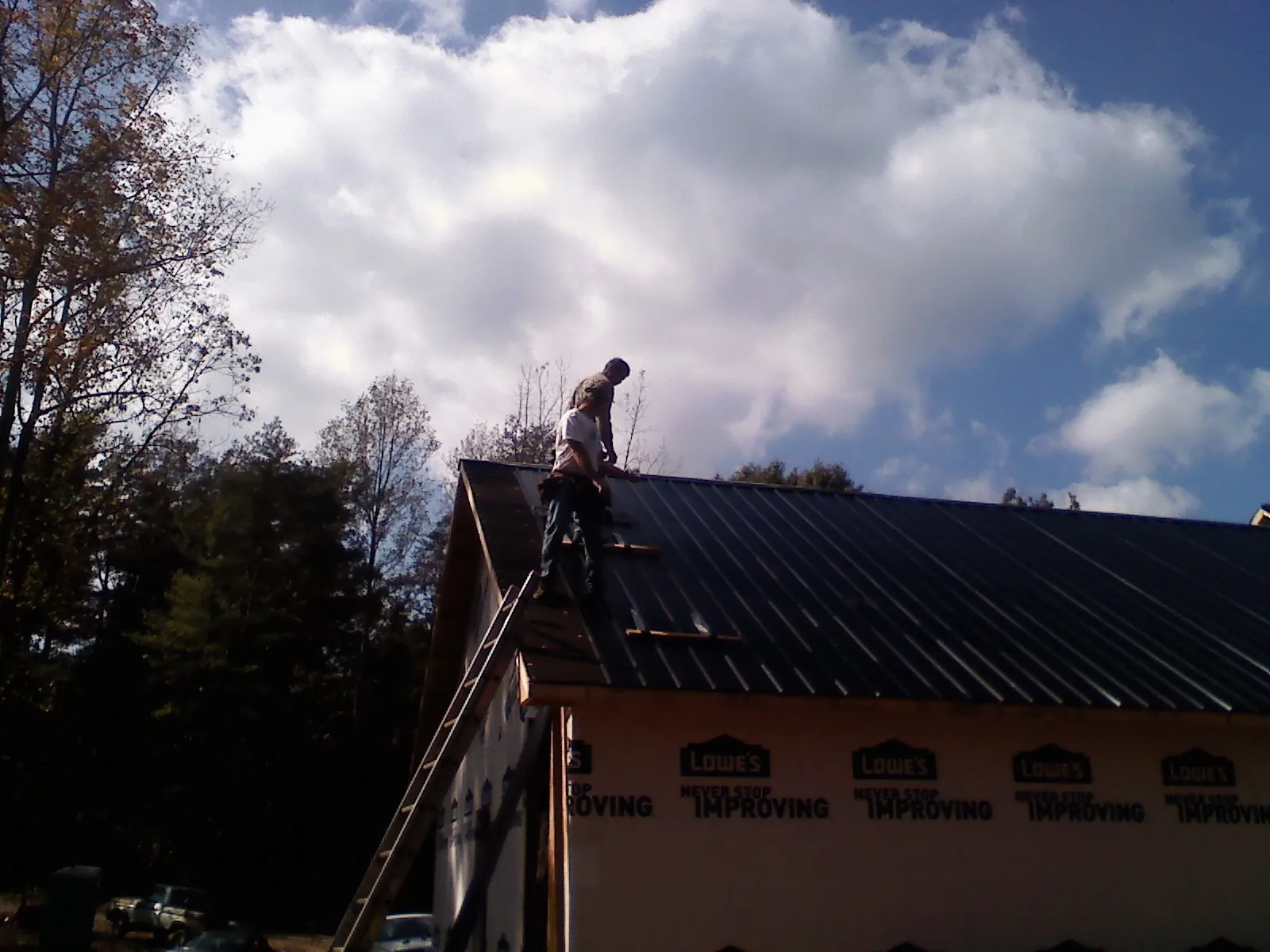 Roofer fastening dark metal panels high against a cloudy sky, from a Roof Inspection job in Stevens