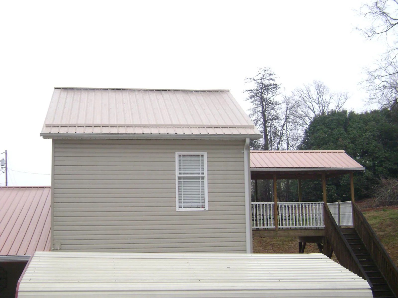 Tan metal roofs on a two story addition and attached porch, from a Roof Replacement job in Stevens